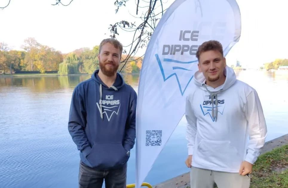 Zwei Ice Dippers im Hoodie am Berliner Ufer, dahinter die Beachflag der Community